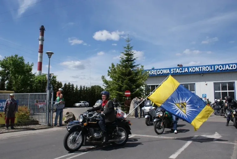 Motocyklista z flagą rajdu wyjeżdża z placu stacji